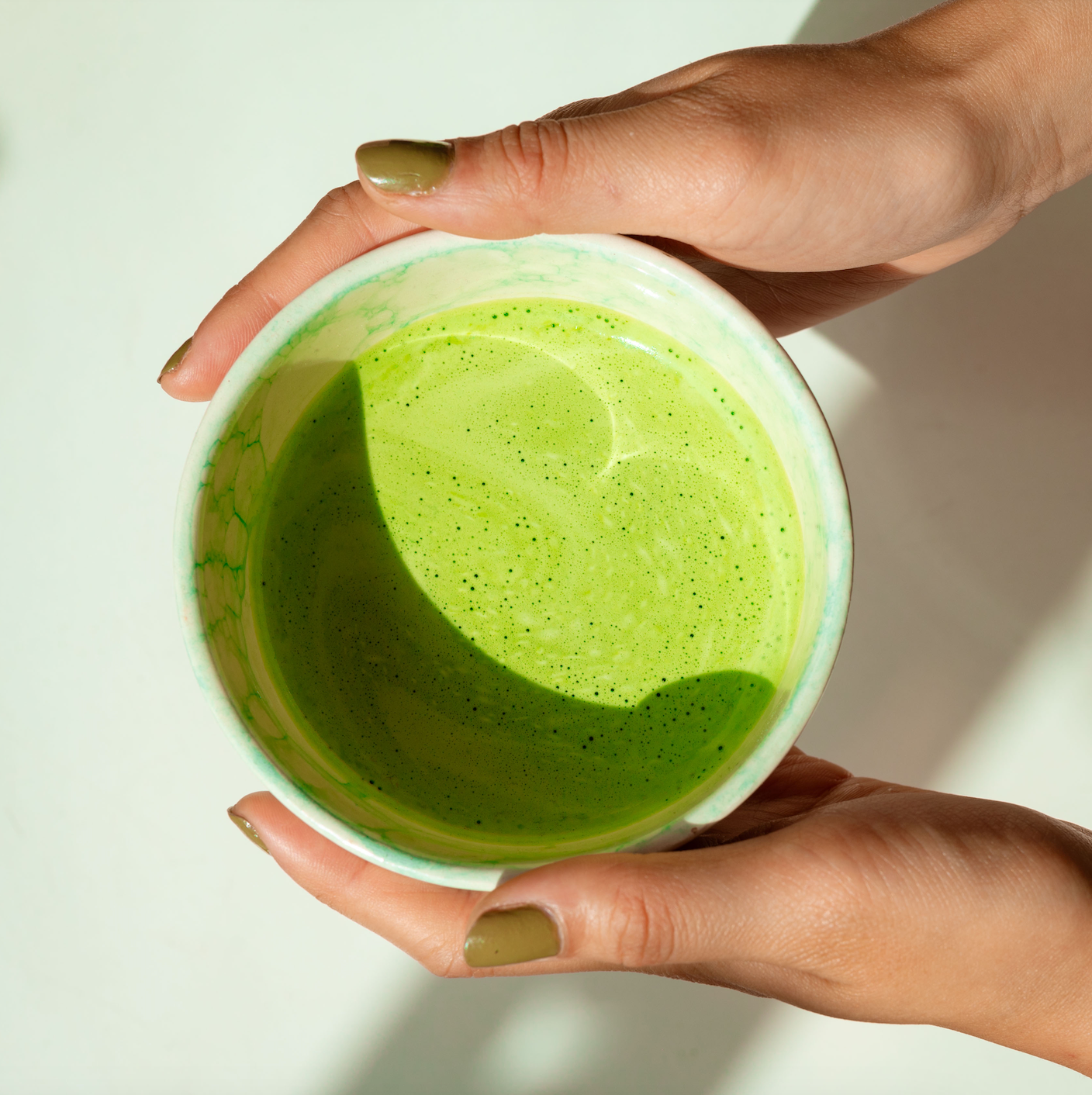 Two hands with Green Nails holding a Cup of Shinrin Matcha